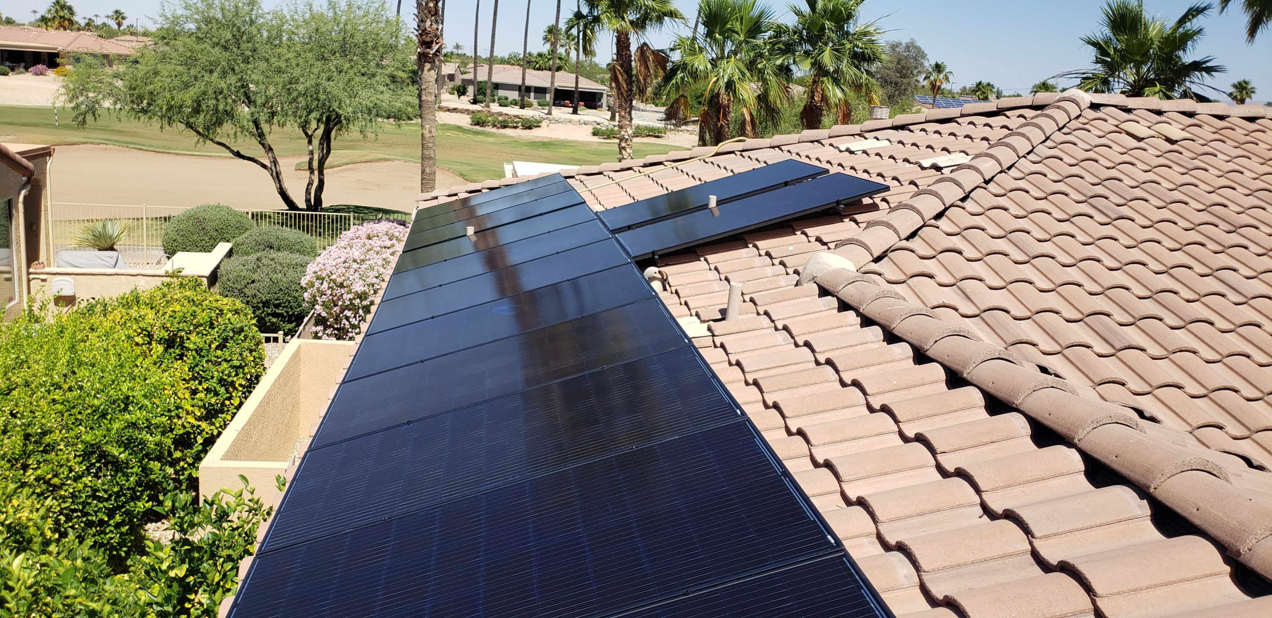 Rooftop solar panels on roof with palm trees and gold course in background.